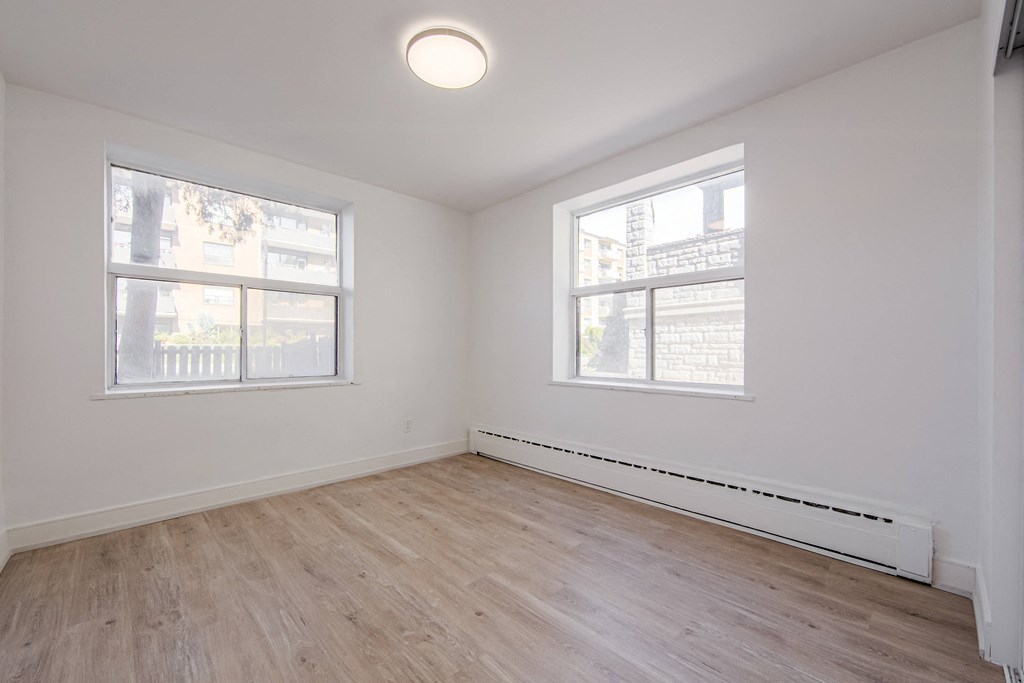 an empty bedroom with wood floors and two windows at 111 Cosburn, East York, ON M4J 2L1