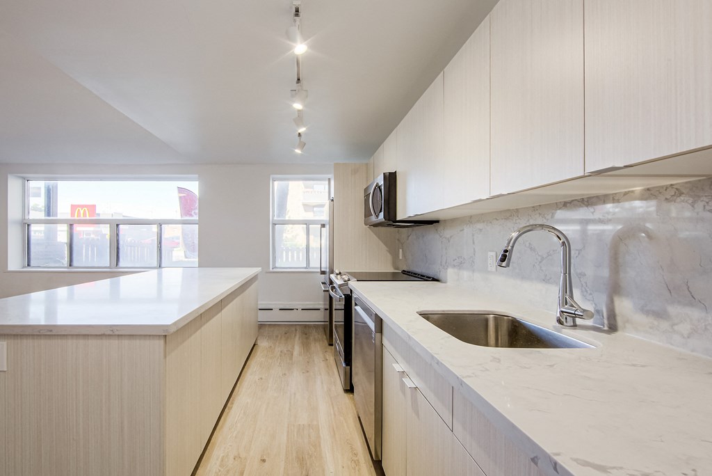 a large kitchen with white cabinets and marble counter tops and a sink at 111 Cosburn, East York