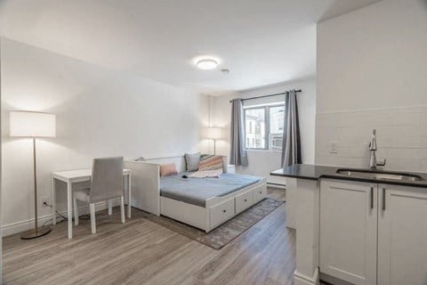 a living room with a bed and a desk and a kitchen