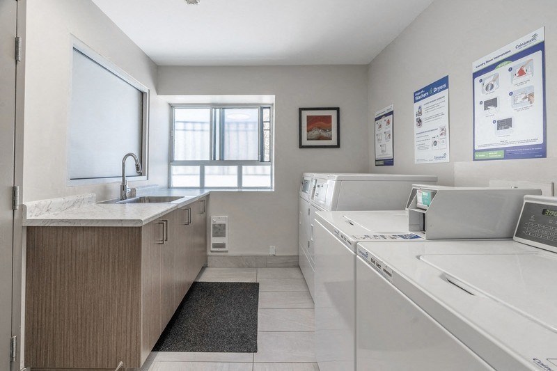 A clean, well-lit laundry room with a washer and dryer, a sink, and a window. at 608 Church Apartments, Toronto