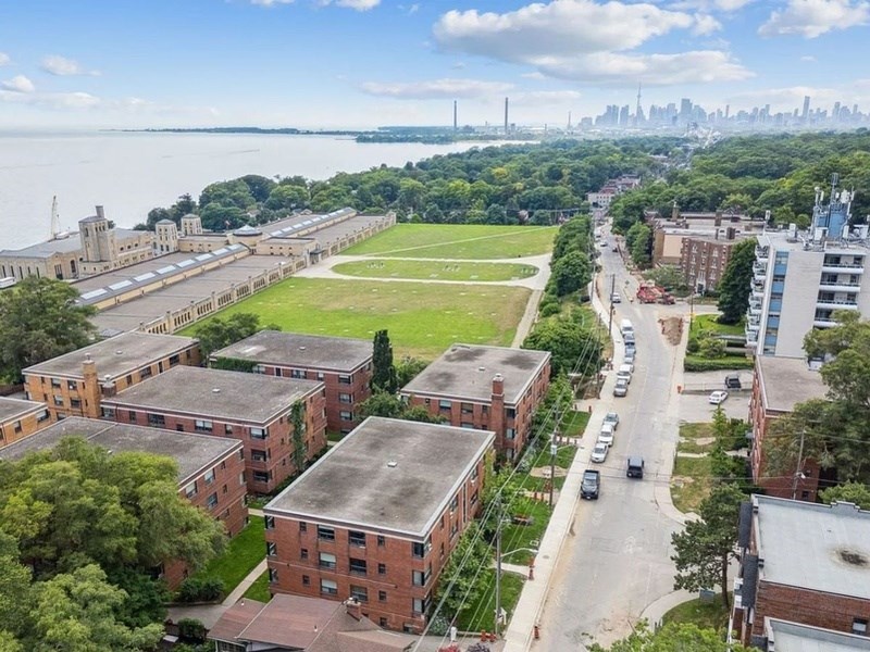 A large building complex with a green field in front and a city skyline in the background.