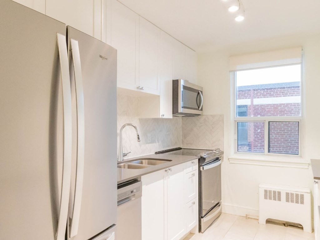 A white kitchen with a refrigerator, microwave, oven, and sink.