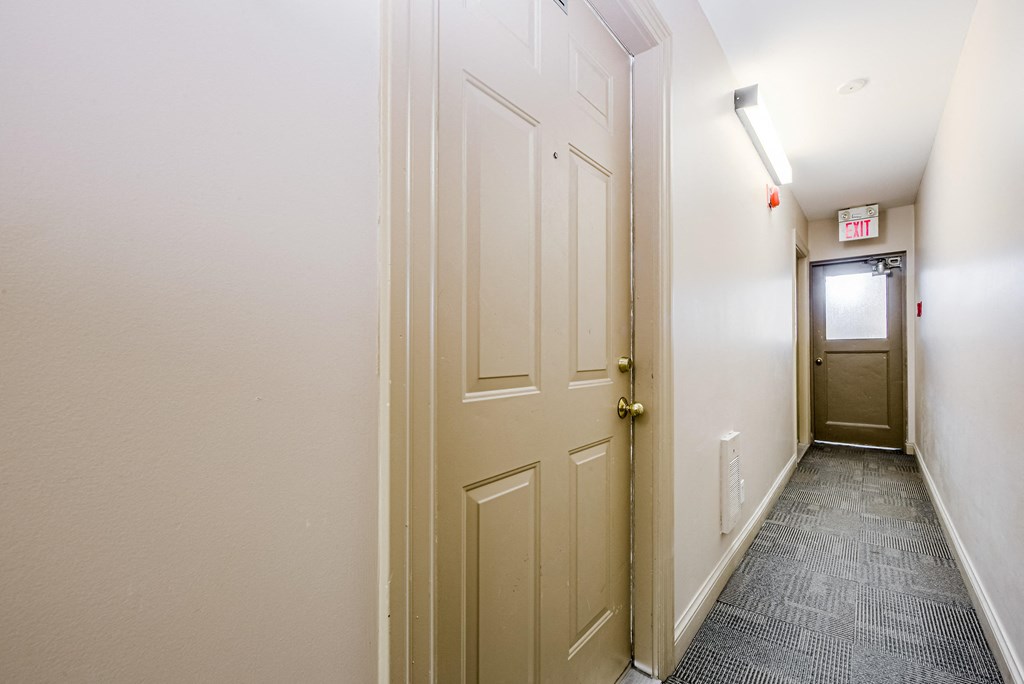 A hallway with a door on the right and a red exit sign above it at 608 Church Apartments, Toronto, ON