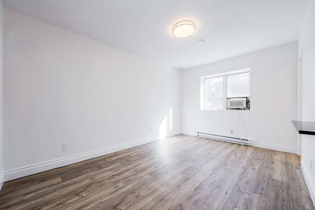 an empty living room with white walls and wood floors and a window at 608 Church Apartments, Toronto, M4Y 2E7