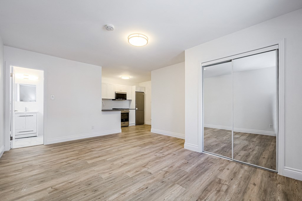 an empty living room with a mirrored closet door and a kitchen at 608 Church Apartments, Toronto, Ontario