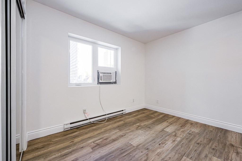 an empty room with white walls and wooden floors and a window at 608 Church Apartments, Ontario