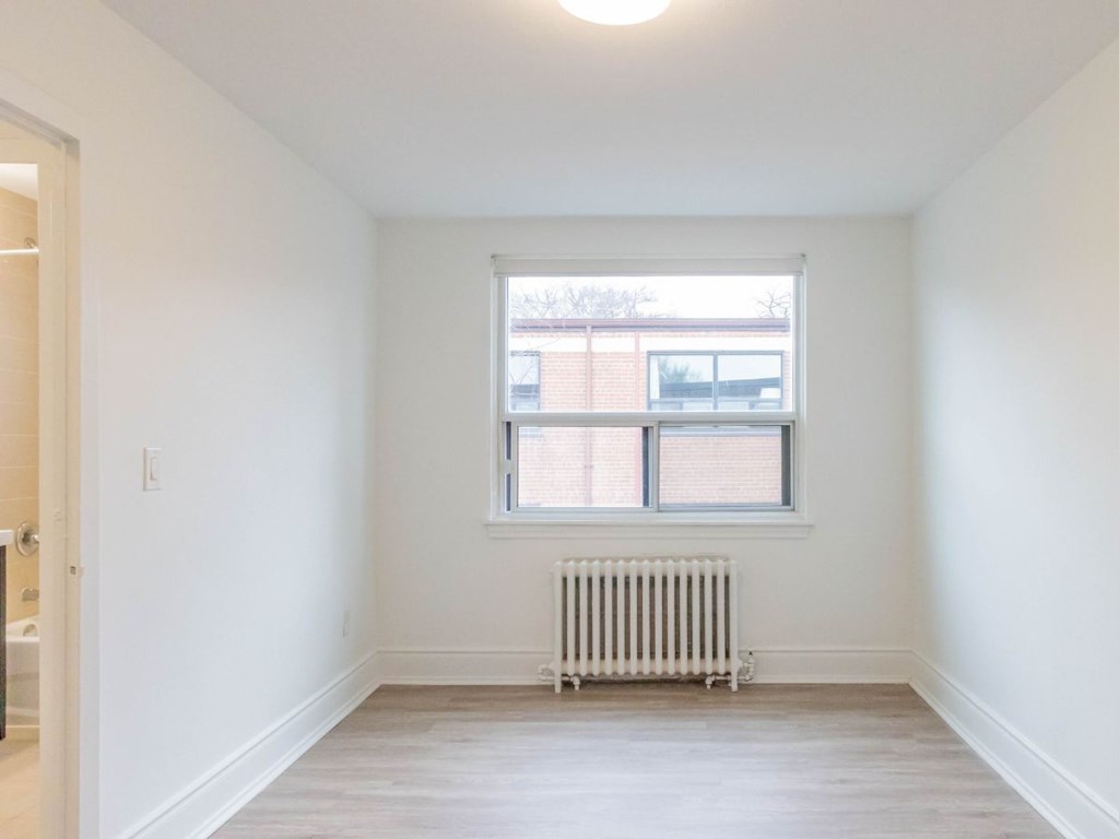 A white room with a window and a radiator on the floor.