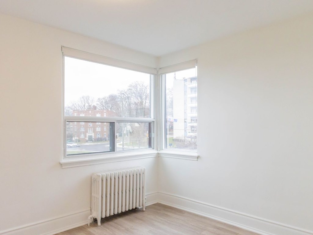 A white room with a window and a radiator on the floor.