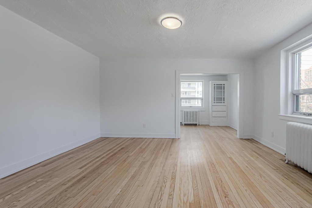 the living room and dining room of an apartment with white walls and wood floors