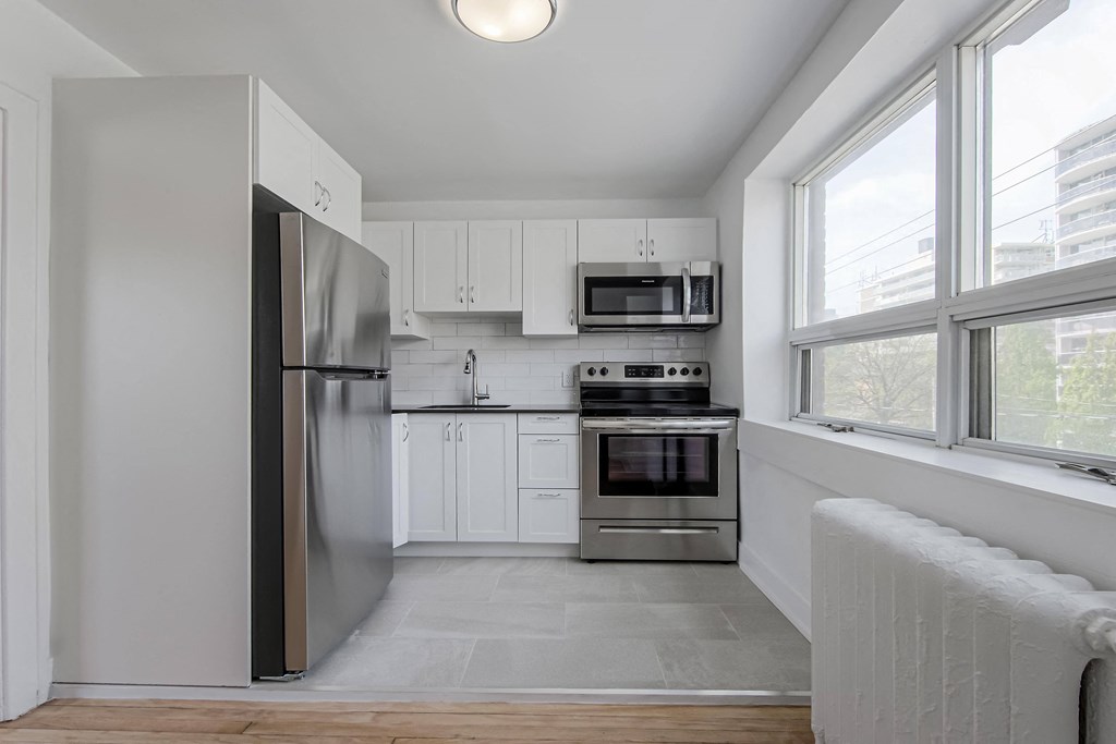 a white kitchen with stainless steel appliances and large windows