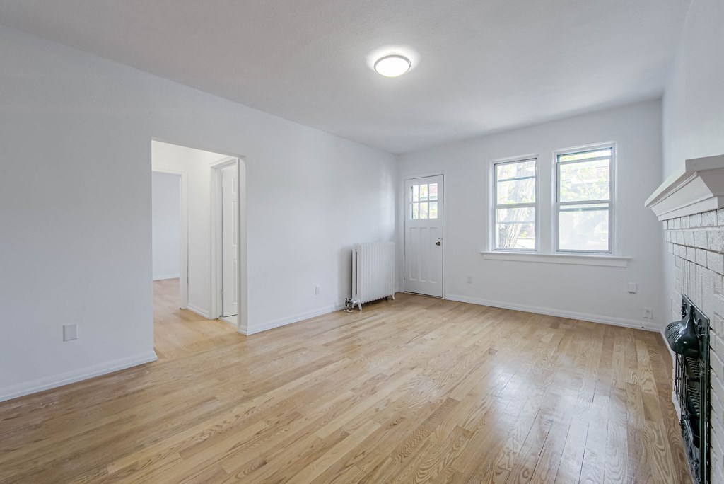 a living room with white walls and wood floors and a fireplace at 83-85 Silver Birch, Toronto, M4E 3L2