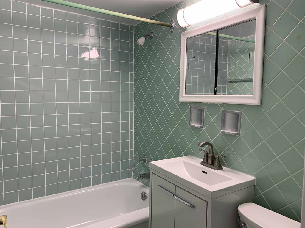 a bathroom with green tiles and a sink and a bath tub
