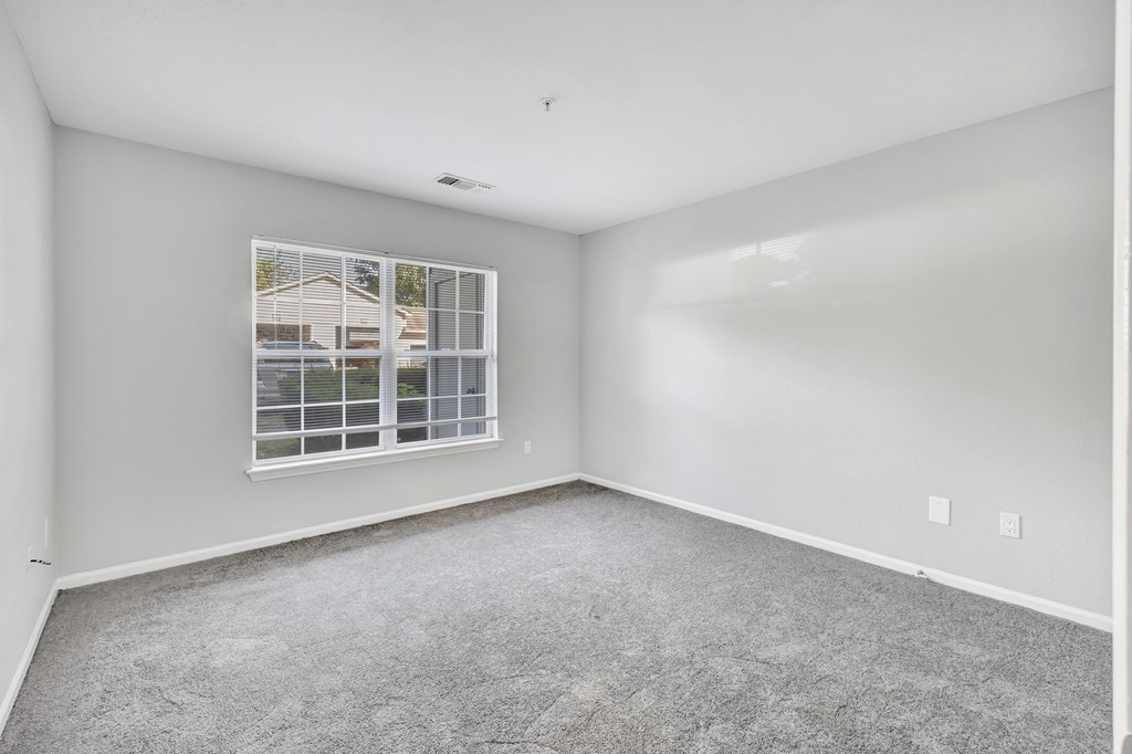 A room with a carpeted floor and a window showing a house outside.