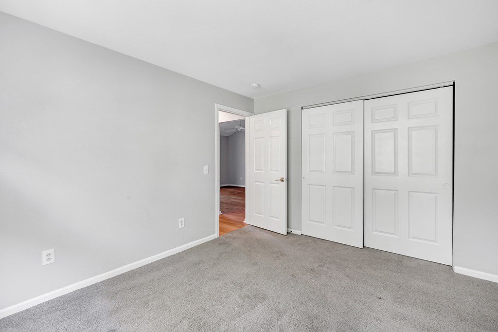 A room with white walls and a carpeted floor with a white door on the right.