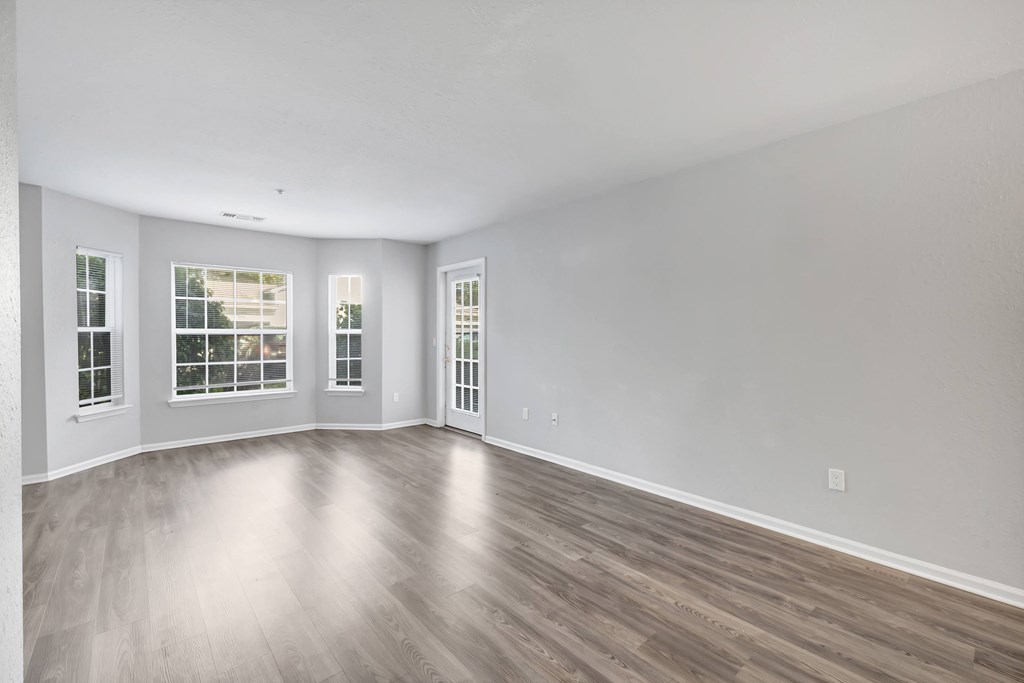 A spacious room with wooden flooring and three windows.