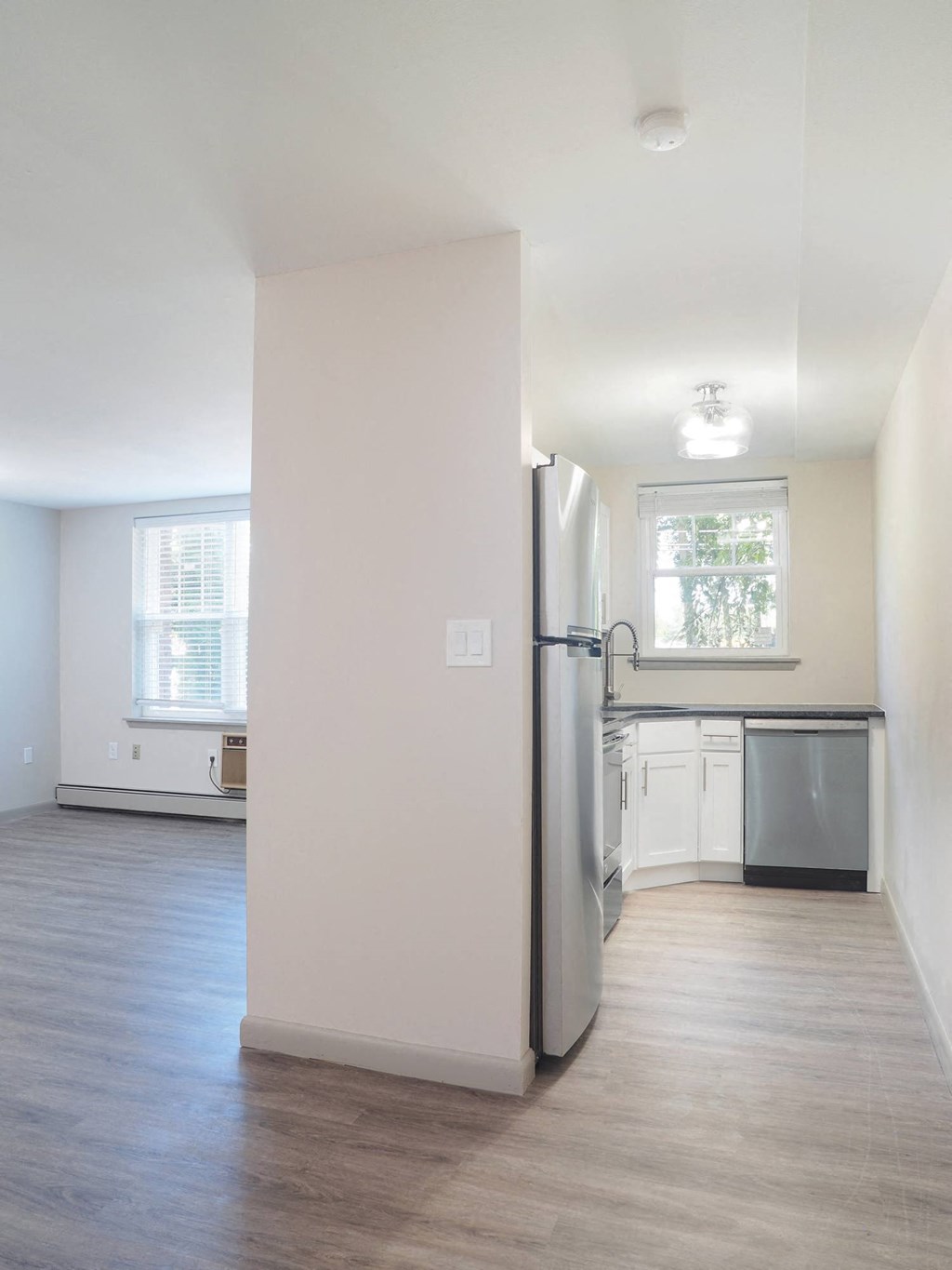 an empty kitchen with white walls and a stainless steel refrigerator