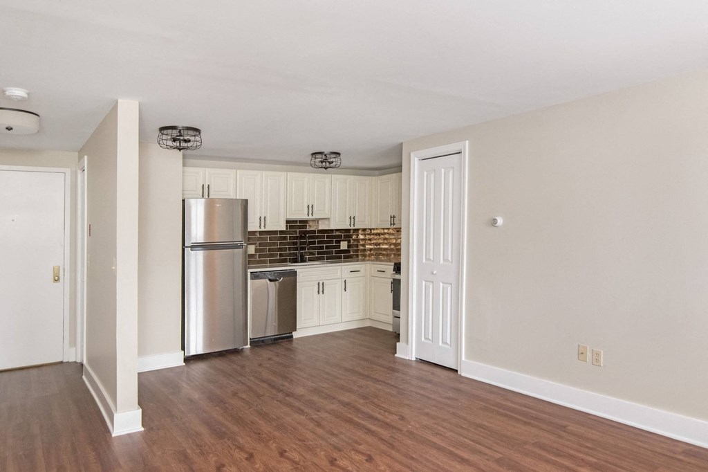an empty living room with a kitchen with stainless steel appliances