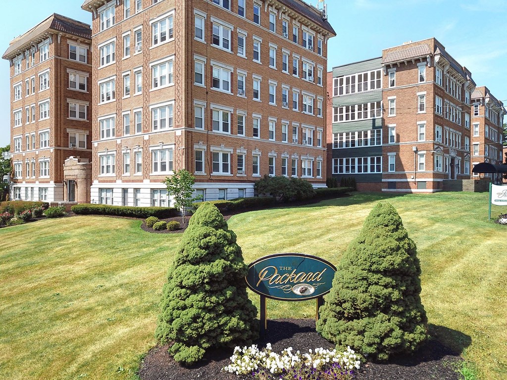 a large brick building with a sign in front of a lawn and trees