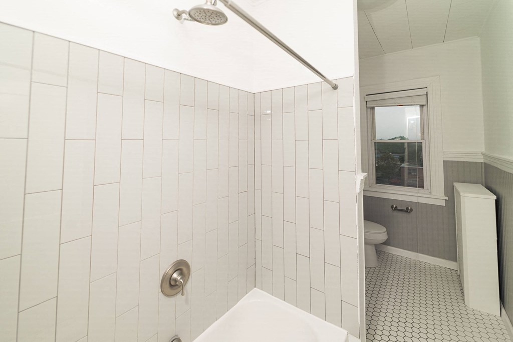 a white tiled bathroom with a tub and a toilet