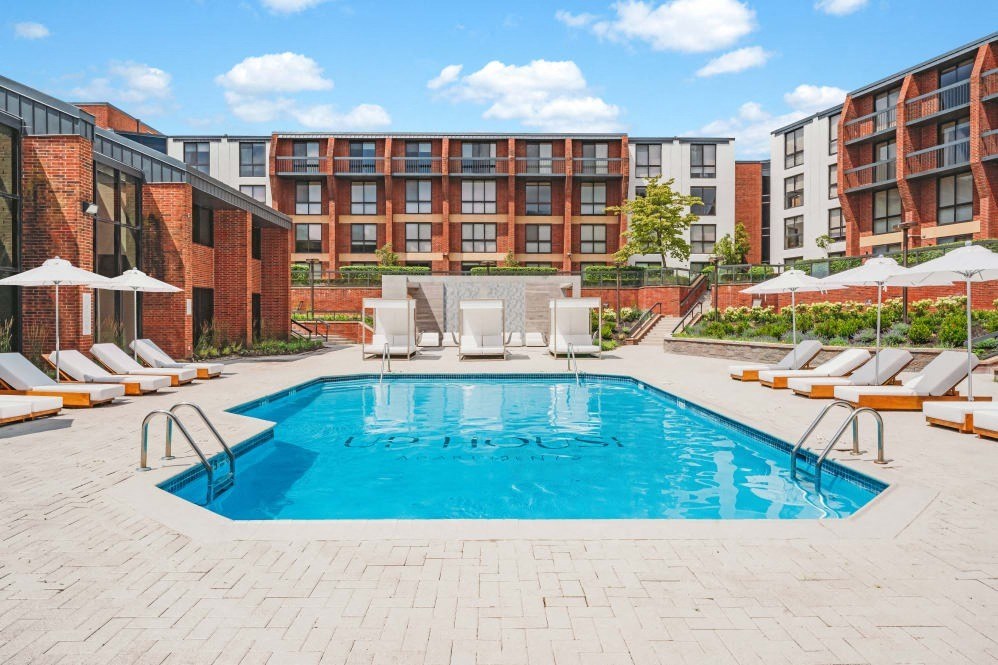 a pool with chairs and umbrellas in front of an apartment building