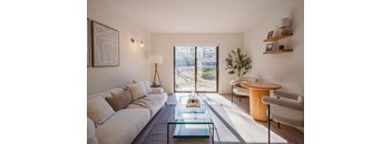 A living room with a white couch, a glass coffee table, and a large window.
