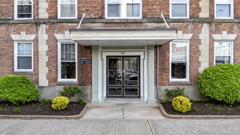 A building with a white door and windows with bushes in front.