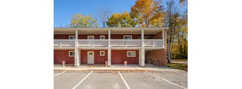 A red building with a white balcony and a parking lot in front.