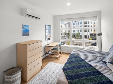 A bedroom with a bed, desk, and window overlooking a street.