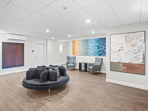 A living room with a grey couch and a painting on the wall.