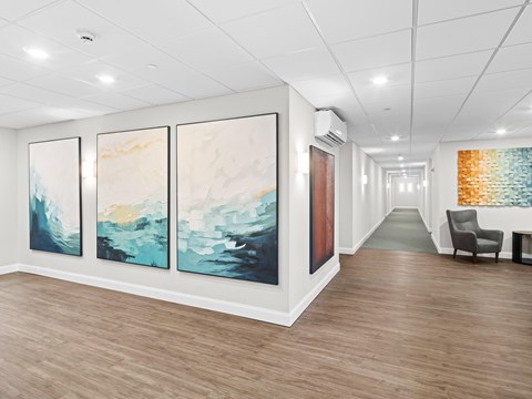 A hallway with three paintings on the wall and a chair on the right.