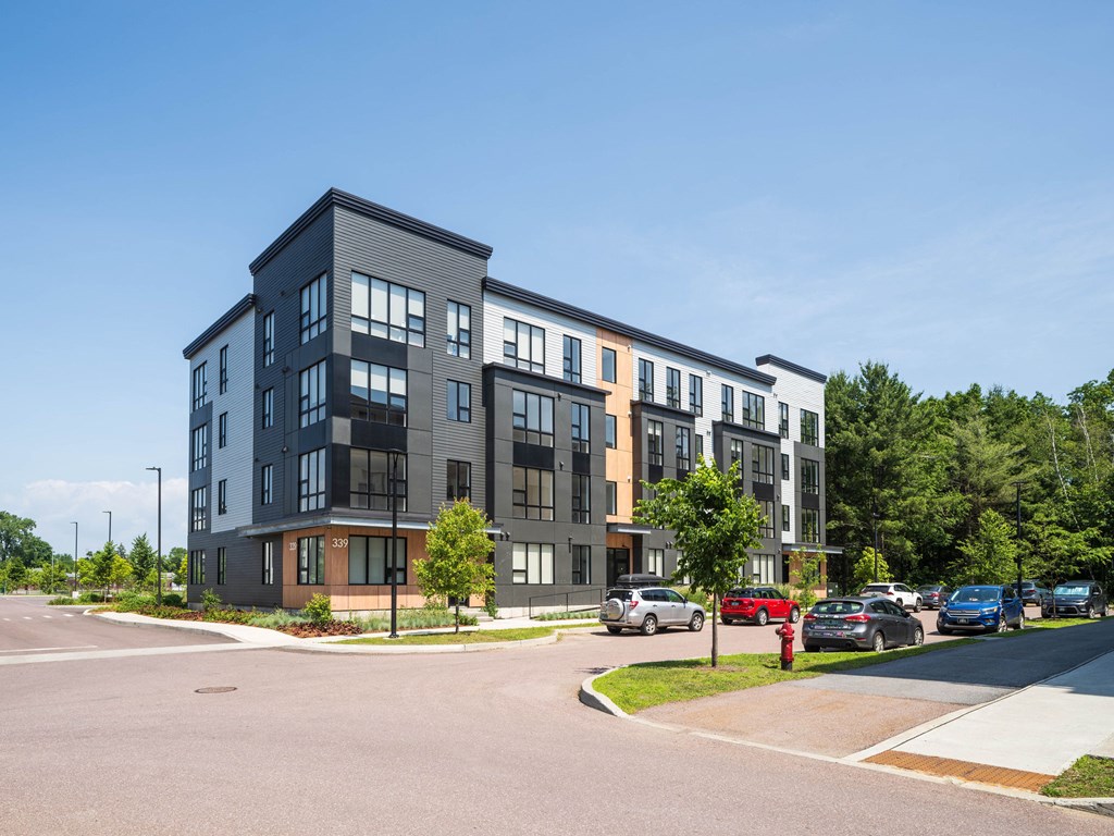 A modern multi-story apartment building with cars parked in front.
