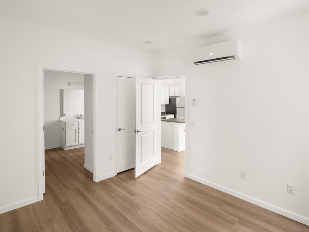A room with a kitchen in the background and a white door open to a hallway.