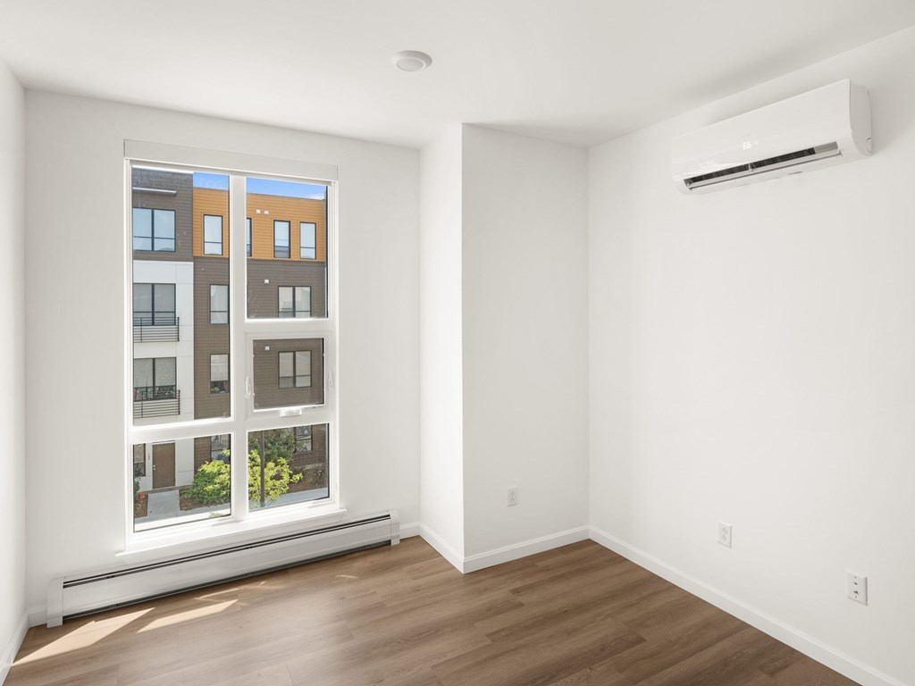 A room with a window showing a building outside and a wall-mounted air conditioner.