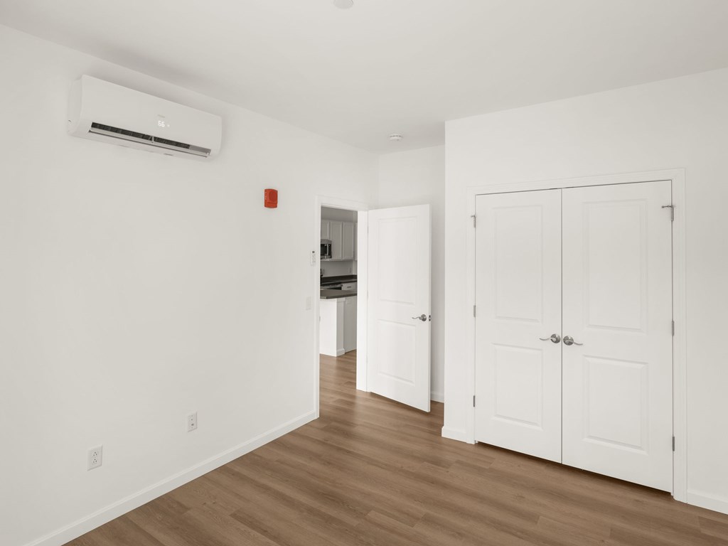 A white room with a wood floor and a wall-mounted air conditioner.