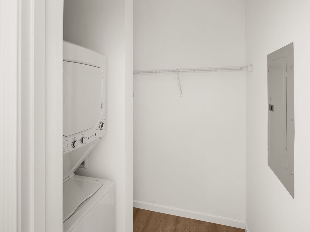 A white dryer is in a small room with a white wall and a white door.