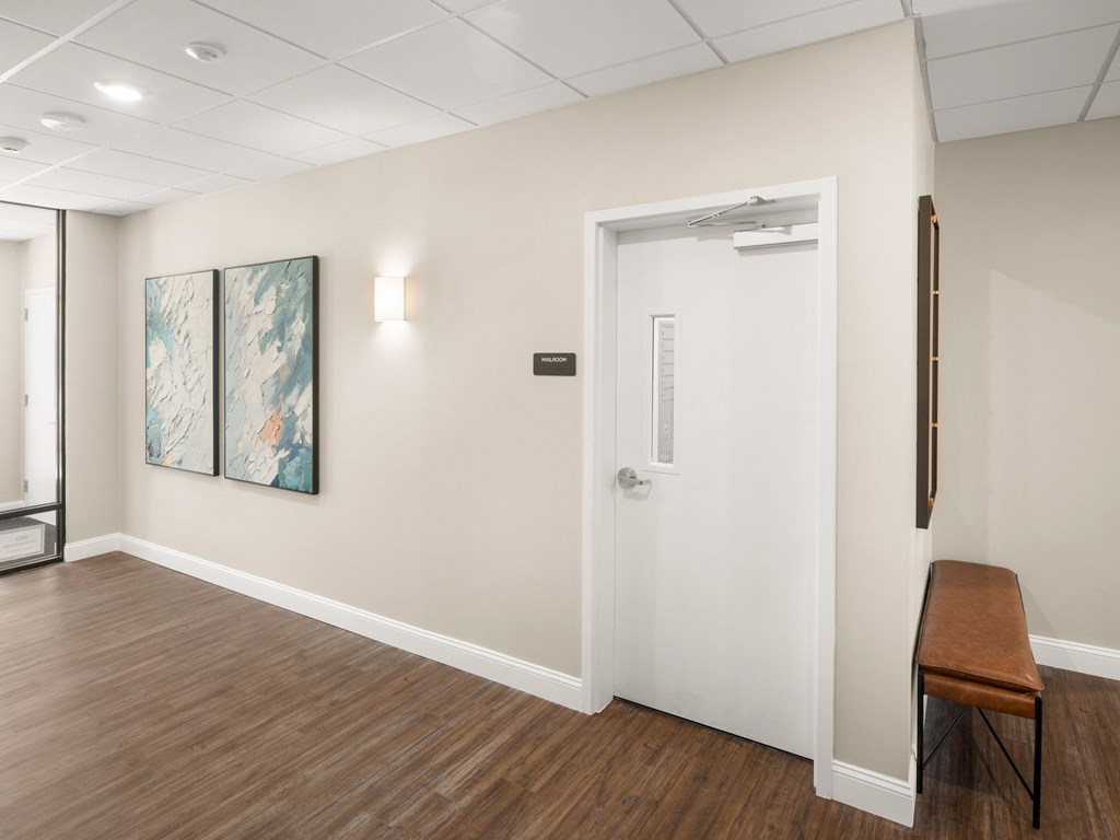 A hallway with a white door, a bench, and two paintings on the wall.
