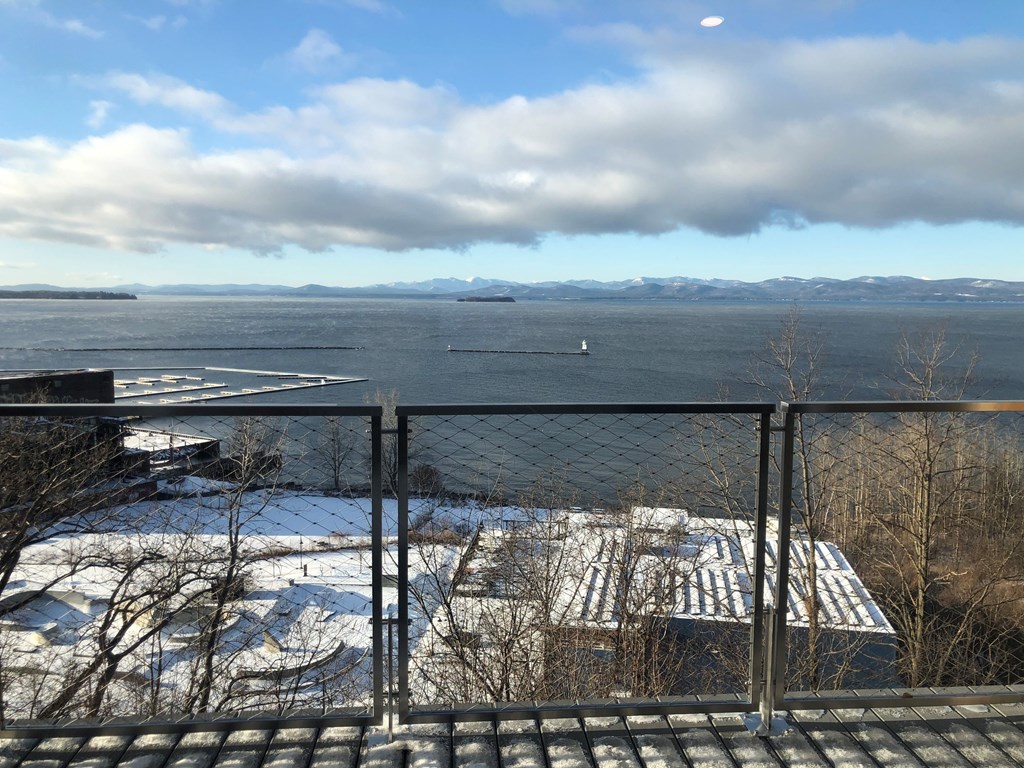 A view from a balcony overlooking a snowy landscape with a body of water and mountains in the distance.