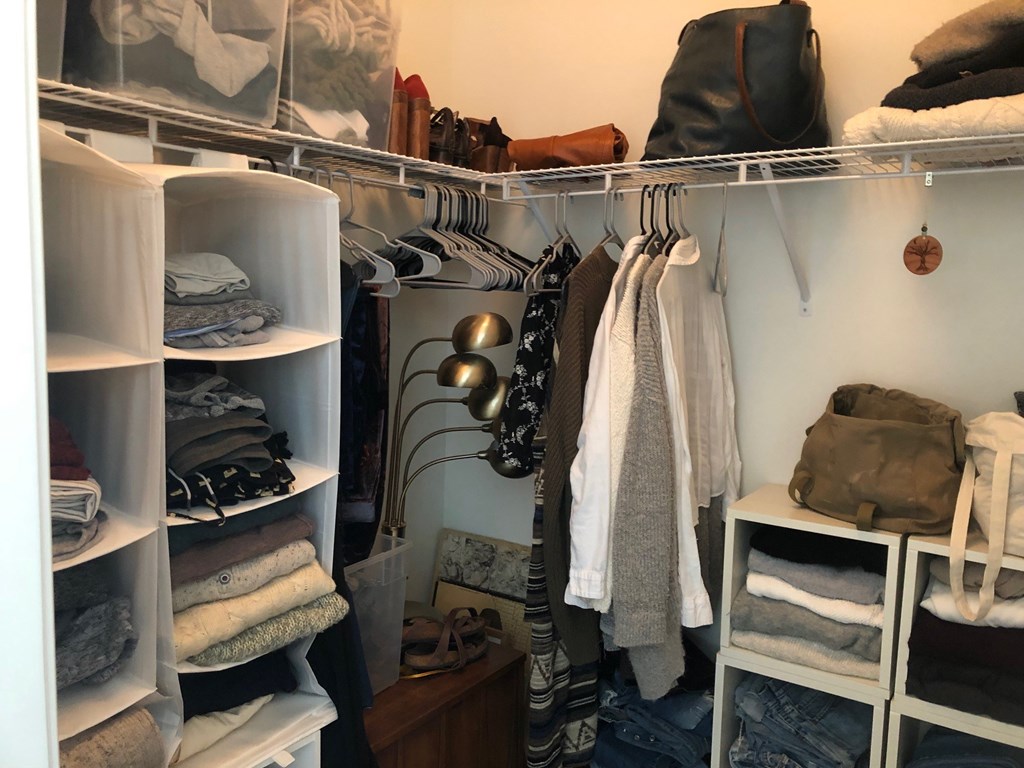 A white closet with clothes and bags.