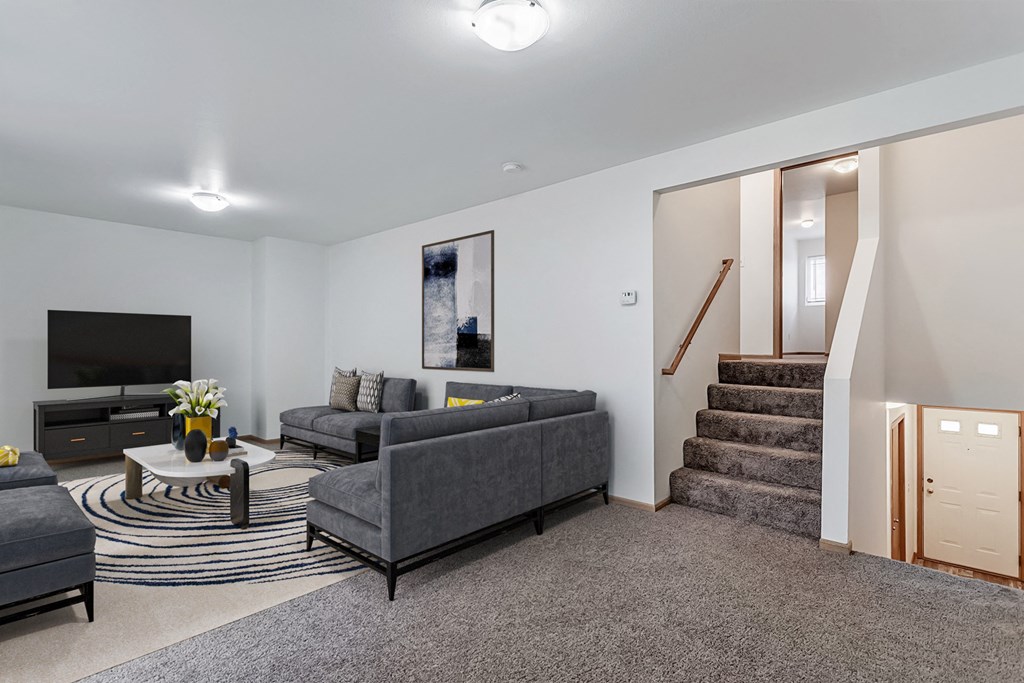 A living room with a grey couch and a staircase.