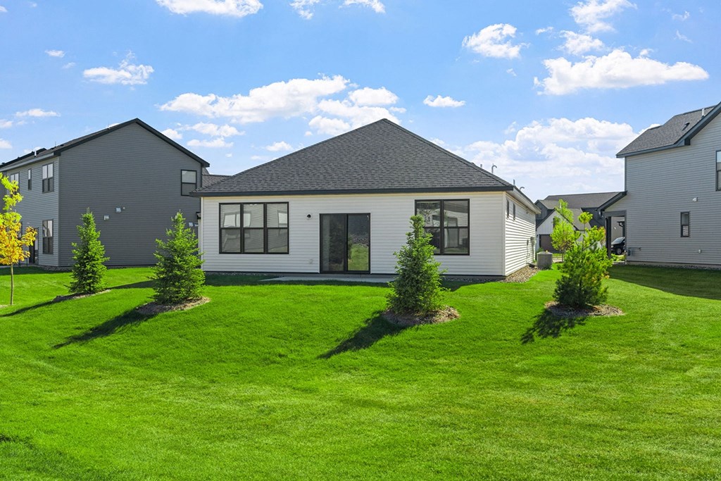 the front of a house with a green lawn and some small trees