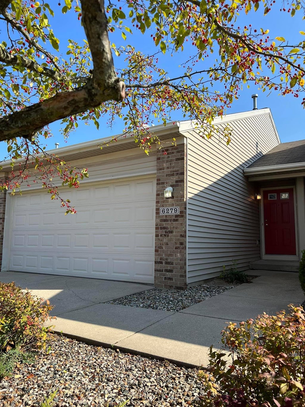 A house with a red door and a garage door is surrounded by trees and plants.