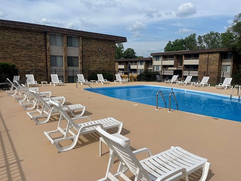 A row of white chairs are lined up on a tan pool deck.