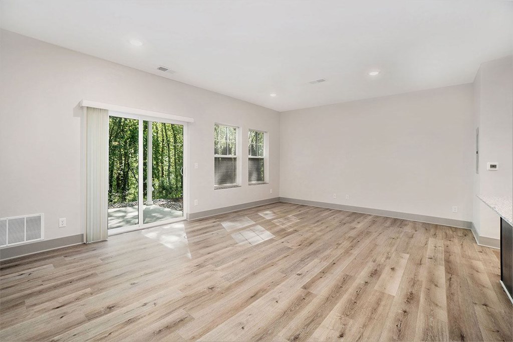 A spacious room with wooden flooring and sliding glass doors leading to a wooded area.