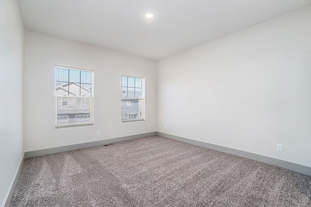 A room with a carpeted floor and two windows.