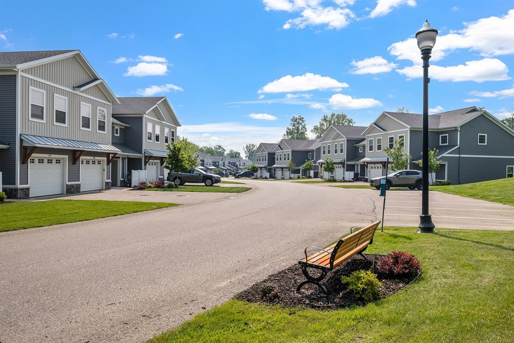A street view of a residential area with houses on both sides and a bench in the foreground.