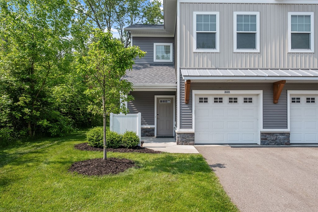 A grey house with a white garage door and a tree in front.