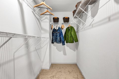 a walk in closet with white walls and clothes hanging on a rack