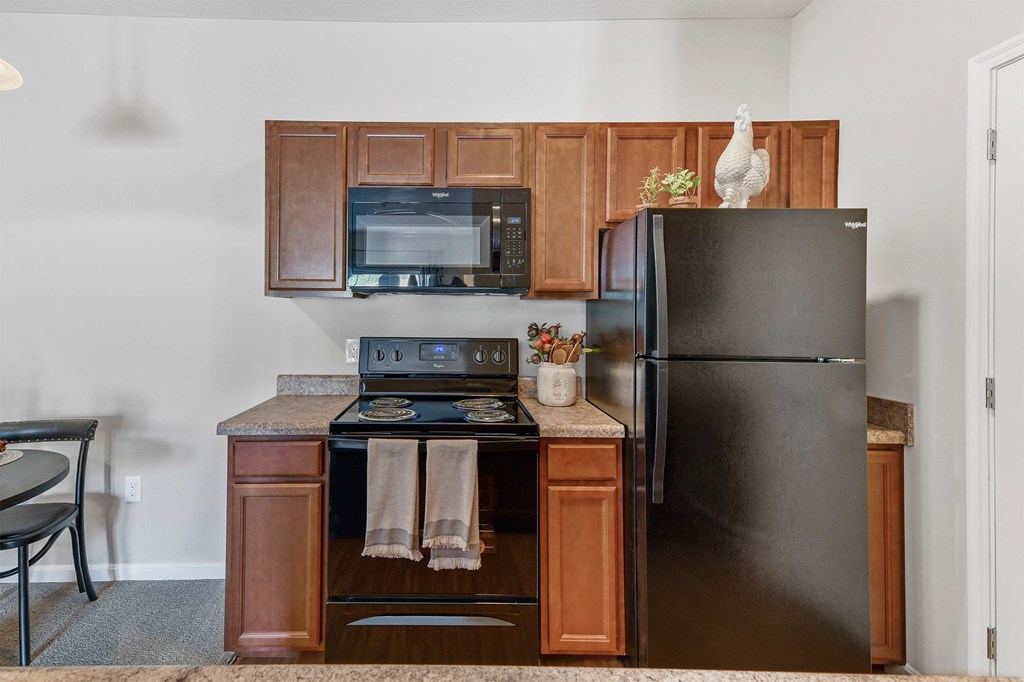 A black refrigerator is in a kitchen with wooden cabinets.