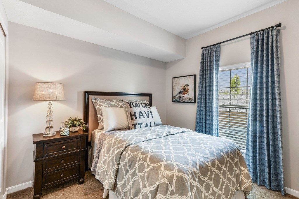 A bedroom with a bed, nightstand, and window with curtains.