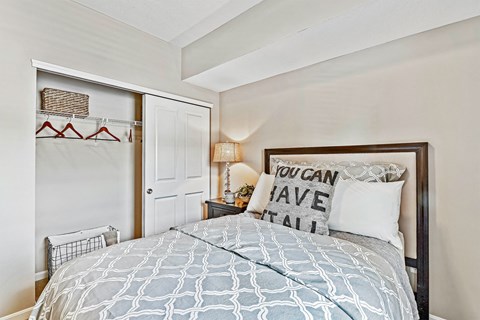 A bedroom with a bed, a lamp, and a pillow that says "You can have it all".